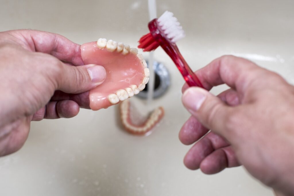 Cleaning and washing of the teeth dentures in the sink with the running water and the toothbrush